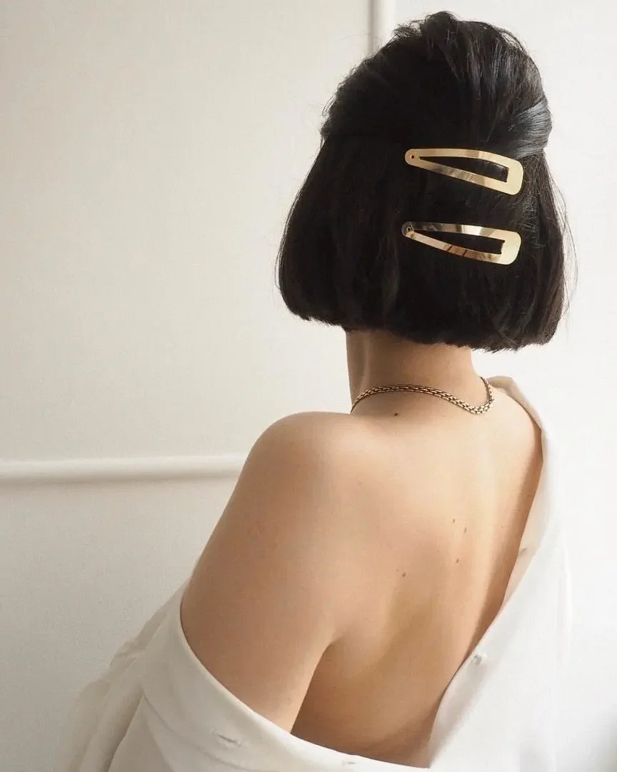 A blunt black bob is pinned half-up with three slim gold clips stacked across the back